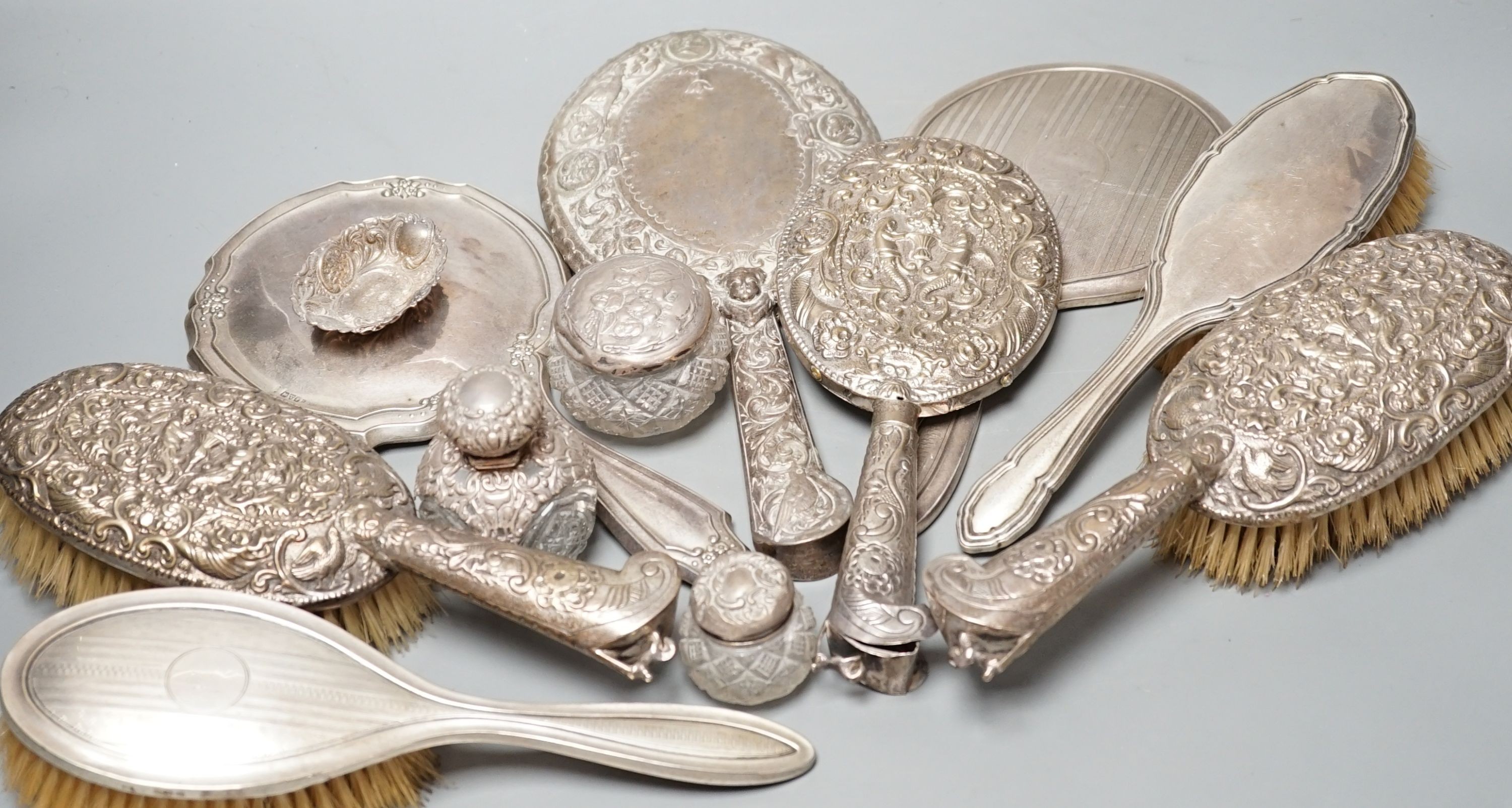 A mixed collection of four silver mounted vanity mirrors, four assorted clothes brushes, (including set of three), three silver mounted glass jars and a small silver dish.